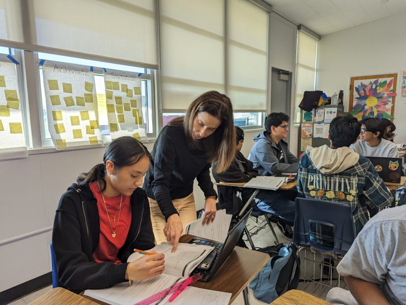 A teacher helps a student with a math workbook assignment.